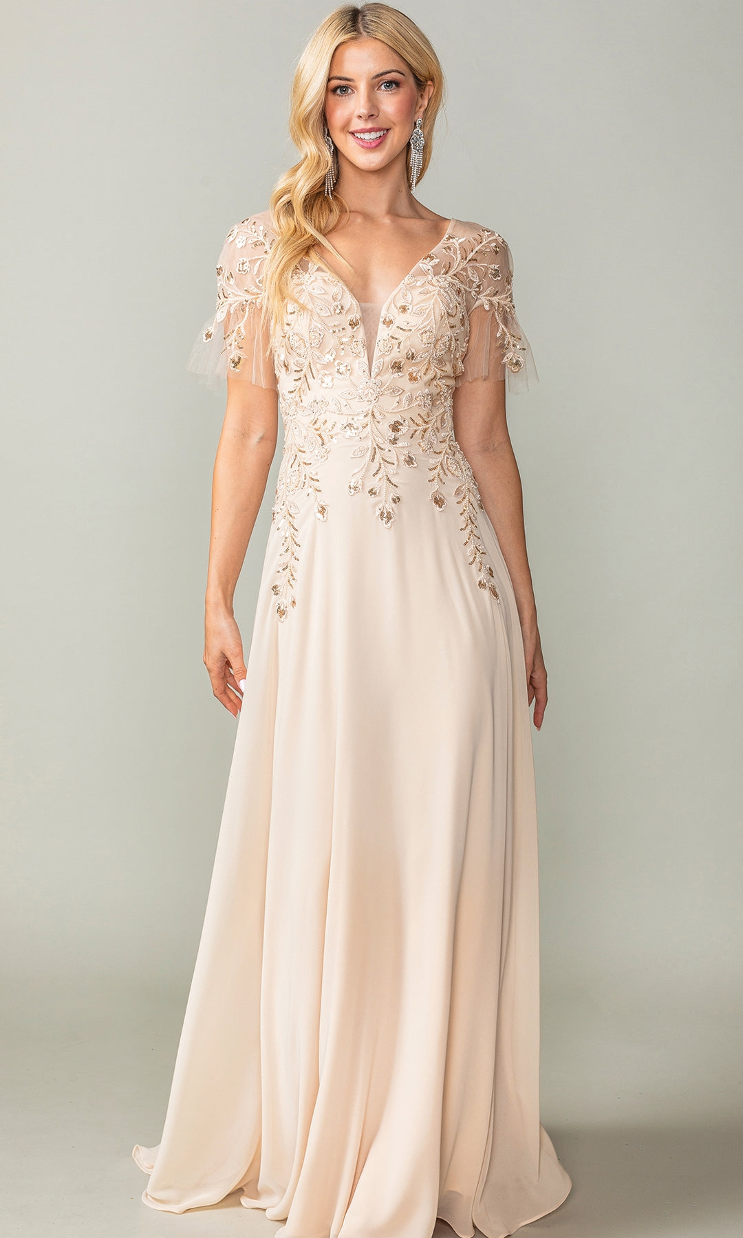 A woman poses against a plain background in the Sheer Short-Sleeve Prom Dress: Dancing Queen 4378, a floor-length light beige gown featuring beaded floral embroidery on the bodice and short sheer sleeves.